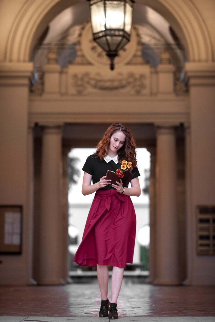 Girl in red skirt reading journal while walking through large grand hallway