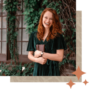 Author K.T. Jay laughing and holding journal in front of rustic house with vines.