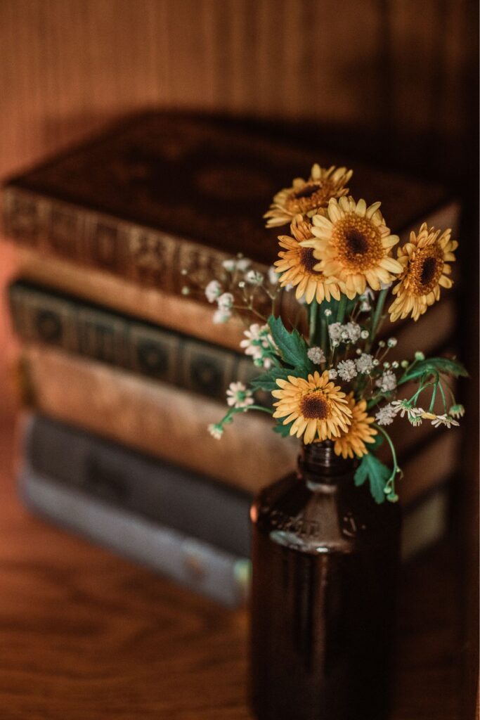 Yellow daisies in a brown vase with a stack of old books in the background.